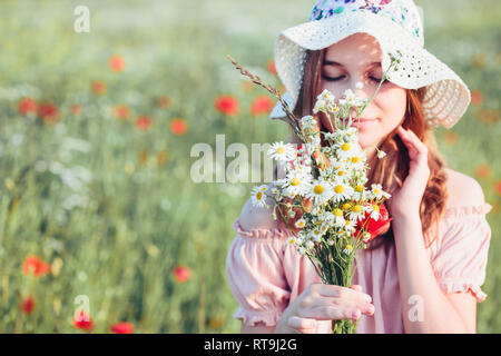 Beautieful junge Mädchen im Bereich der wilden Blumen. Jugendmädchen Ernte der Blumen auf der Wiese, holding Blumenstrauß. Sie trägt Hut Stockfoto