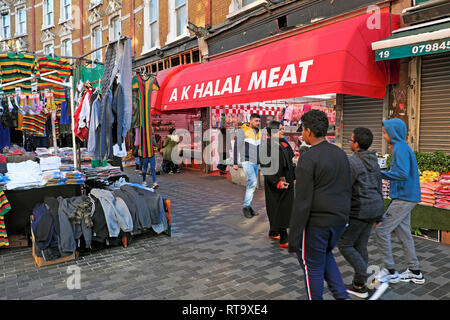 Menschen gehen vorbei AK Halal Fleisch Metzgerei Store & Kleidung Stall, Brixton Street Market Electric Avenue Brixton London SW9 England UK KATHY DEWITT Stockfoto