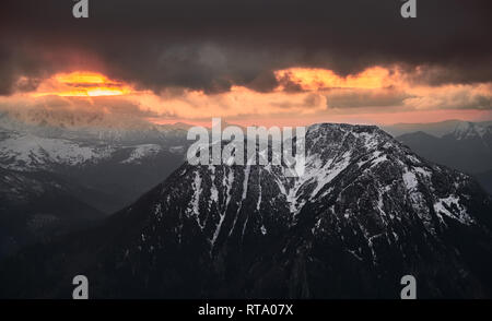 Sonnenuntergang Stanzen durch dunkle Wolken über einem Berg Stockfoto