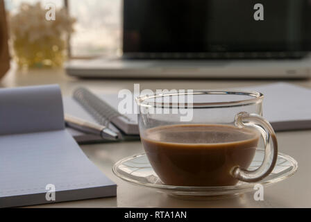 1 Tasse Kaffee neben dem Notebook und mit Blumen und Laptops auf einem weißen Schreibtisch platziert Stockfoto