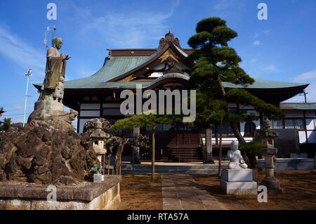 Traditioneller japanischer buddhistischer Tempel mit kunstvoller Holzarchitektur, Steinstatuen und gepflegten Kiefern unter einem klaren blauen Himmel. Ein heiterer und sein Stockfoto