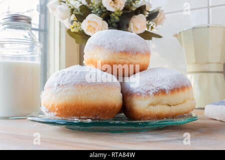 Drei frische Donuts auf eine Glasplatte mit moka Topf, Blumen und Milch Flasche im Hintergrund Stockfoto