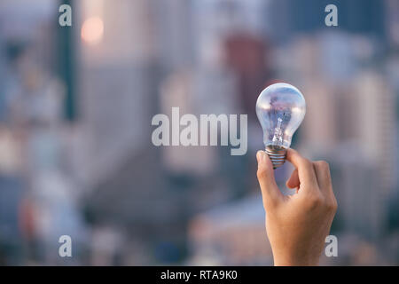 Glühbirne vor Sonnenuntergang städtischen Häuser. Glühlampe transparent Lampe in alternative Solar Energie des Menschen in der Stadt, Stadt, Stadt Nachtleben. Symbol, Konzept der Busi Stockfoto