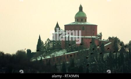 In der Nähe von San Luca Basilika Kirche mit Schnee auf Bologna Hill in Italien mit einem Schwarm Vögel fliegen Stockfoto