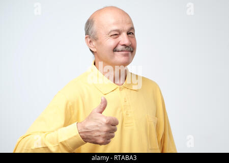 Portrait glücklich im mittleren Alter Mann im gelben Shirt mit Schnurrbart, Daumen hoch. Stockfoto