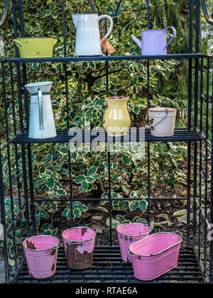 Alte Gießkannen und andere Utensilien und Schiffe außerhalb auf Metall Rack als Dekoration im Garten Stockfoto