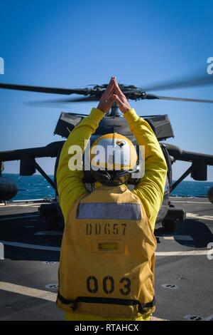 ARABIAN GULF (Feb. 4, 2019) Bootsmann Mate 1. Klasse Daniel Linsalata Signale Befehle an ein UH-60 Black Hawk Hubschrauber, zu Task Force Javelin zugeordnet, auf dem Flugdeck der Arleigh-Burke-Klasse geführte Anti-raketen-Zerstörer USS Mitscher (DDG57). Mitscher ist in die USA 5 Flotte Bereich der Maßnahmen zur Unterstützung der Marine im Einsatz für die Stabilität und Sicherheit in der Region zu gewährleisten und verbindet das Mittelmeer und den Pazifischen Raum durch den westlichen Indischen Ozean und drei strategischen Punkten ersticken. Stockfoto