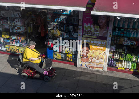 Eine behinderte Frau fährt ihre Mobilität scooter Vergangenheit eine Schönheit und der Frauen 'Zubehör Shop in der Walworth Road, am 27. Februar 2019 in London, England. Stockfoto