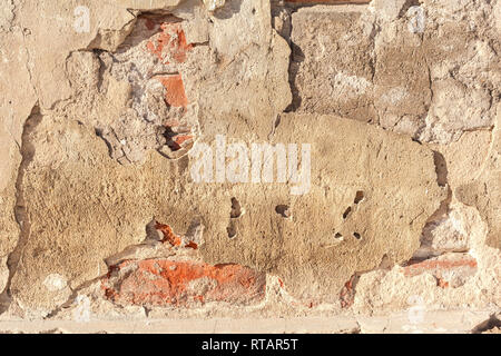 Stuck auf eine Wand. Der Putz fällt von einer alten Mauer. Alte Risse und die Mauer aus roten Ziegeln mit Resten von Gips ruiniert. Grunge Hinterg Stockfoto