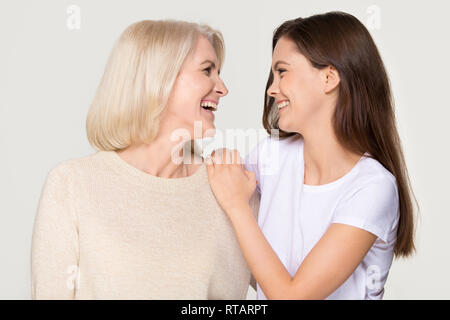 Glückliche junge Tochter umarmen reife Mutter Lachen auf Hintergrund isoliert Stockfoto