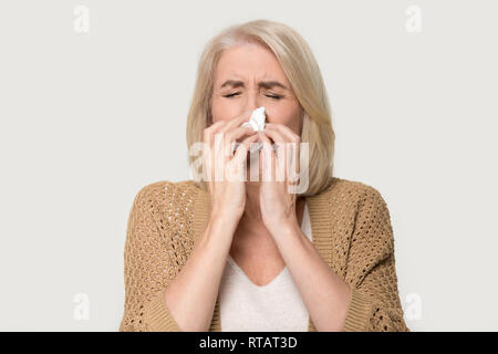 Kranke allergische alte Frau blasen runny Nase auf Hintergrund isoliert Stockfoto