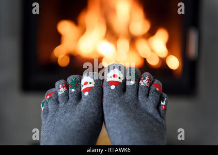 Kamin und Mädchen Füße in den lustigen Wollsocken im Vordergrund. Hygge Konzept Stockfoto