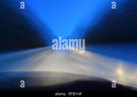 Pov-shot durch die Windschutzscheibe eines Autos fahren auf einer verschneiten Feldweg durch einen Wald in der Dämmerung Stockfoto