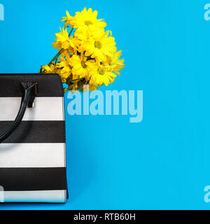 Konzept der Geschenk für einen Business Woman: weibliche Zubehör schwarze und weiße Tasche gelbe Blüten auf blauem Hintergrund. Valentinstag Geburtstag Geschenk Stockfoto