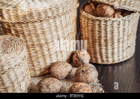 Ganze Walnüsse in Korb und auf einem dunklen Holztisch verstreut, Platz für Text. Gesunde Ernährung Konzept. Stockfoto