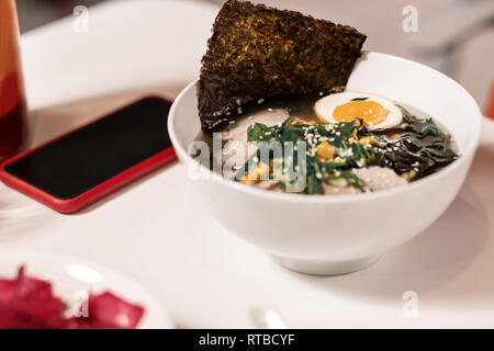 Schließen Sie herauf Foto der Schüssel mit Ramen und Smartphone neben sie auf den Tisch. Stockfoto