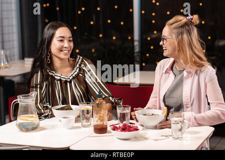 Zwei weibliche Freunde sitzen und plaudern mit Begeisterung im Cafe über Mittag. Stockfoto