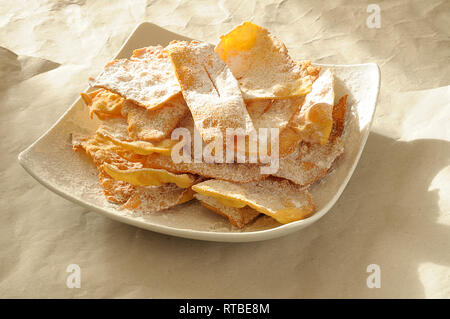 Italienischen Karneval sweet Fried, genannt Frappe oder Chiacchere. In der Regel homeade Kochen auf Karneval feiern. Quadratische Platte mit Hintergrundbeleuchtung von Sun Stockfoto