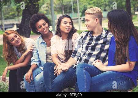 Gruppe der Kuehlung lateinamerikanischen und afrikanischen Jungen Erwachsenen im Freien auf dem Campus der Universität Stockfoto