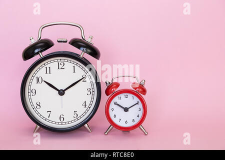 Zwei rote und schwarze retro Alarm Clocks auf einem rosa Hintergrund mit Freiraum für Text Stockfoto