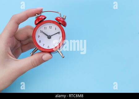 Mädchen, dass eine Red retro Wecker zeigt zehn Uhr zehn Minuten auf dem Zifferblatt, auf blauem Hintergrund. Konzept - Zeit ist Geld Stockfoto