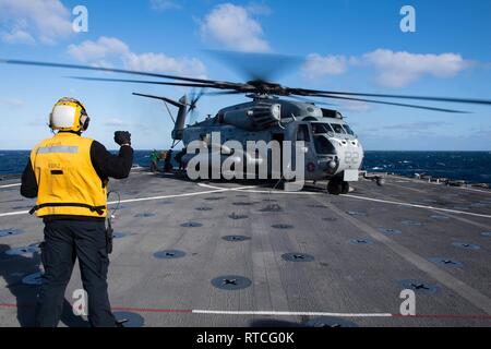 Pazifik (Feb. 16, 2019) der Bootsmann Mate 2. Klasse Patrick Obrien, aus Boston, Signale an das mit der CH-53E Super Stallion, Marine schweren Helikopter Squadron (HMH) 465 befestigt, auf dem Flugdeck der Harpers Ferry-Klasse amphibische Landung dock Schiff USS Harpers Ferry (LSD 49). Harpers Ferry ist unterwegs die Durchführung von Routineaufgaben als Teil der USS Boxer Amphibious Ready Group (ARG) im östlichen Pazifik. Stockfoto