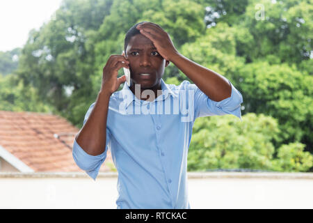 Schockiert afrikanische amerikanische Geschäftsmann am Telefon im Freien in Afrika Stockfoto