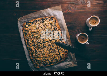 Blick von oben auf die frisch gebackenen Wiener Cookies in Quadrate schneiden neben zwei Tassen Kaffee. Leckere hausgemachte Desserts und Getränken. Stockfoto