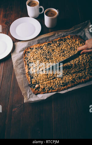 Weibliche Hand schneiden frisch gebackene Plätzchen neben zwei Tassen Kaffee auf braune Holztisch. Stockfoto