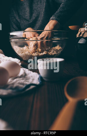 In der Nähe von weiblichen Händen kneten den Teig für Kreis in großen glasschale auf braune Holztisch. Stockfoto