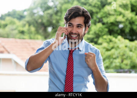 Jubelnde latin Geschäftsmann mit Bart am Handy im Freien Stockfoto