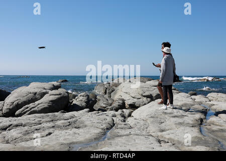 Mann und Frau fliegen und Film eine Drohne UAV über Felsen und Meer auf Kaikoura Halbinsel in der Nähe der Robbenkolonie in der Sommersonne. Neuseeland Südinsel Stockfoto