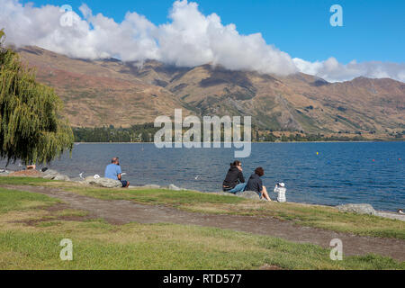 Touristen oder einheimische Sitzen sprechen die Bilder am Strand in der Sonne am Lake Wanaka Neuseeland Südinsel Stockfoto