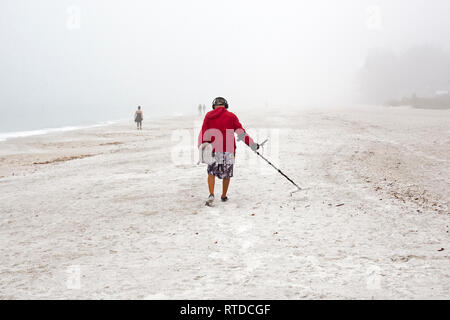 Ein Mann mit einem Metalldetektor am Strand an einem nebligen Tag auf Anna Maria Island, Florida, USA. Stockfoto