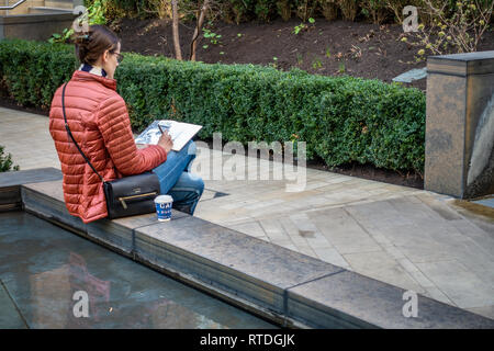 Junge Frau sitzt außerhalb Zeichnung im Innenhof außerhalb von Google UK Corporate Office in Kings Cross, London, England Stockfoto