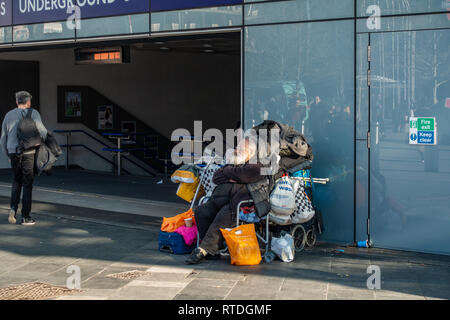 Alten Obdachlosen Mann in seinem Stuhl umgeben von all seinen vielen Reihen am Bahnhof Kings Cross, London, England sitzen Stockfoto