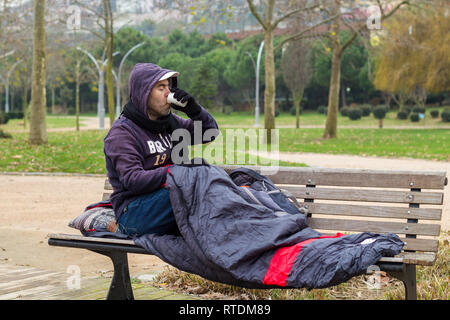 Obdachloser ist Kaffee trinken auf der Werkbank Stockfoto