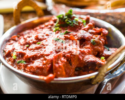 Indisches essen und indische Curry in einem Kupfer Messing serviert orientalische Schale, Hähnchenbrustfilet in Currysauce Zutaten in einen Topf mit der alten Tabelle Stockfoto