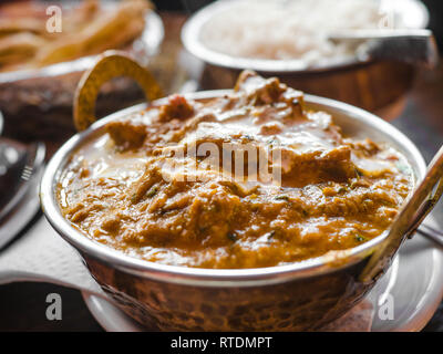 Indisches essen und indische Curry in einem Kupfer Messing serviert orientalische Schale, Hähnchenbrustfilet in Currysauce Zutaten in einen Topf mit der alten Tabelle Stockfoto