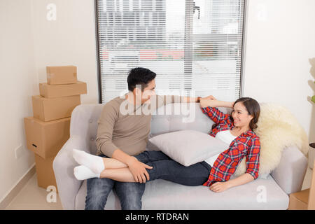 Glückliches Paar entspannt auf einem Sofa, das Spaß am Umzugstag, neugierige junge Hausbesitzer genießen Umzug in ein neues Zuhause, positive lachenden Mann und Frau Stockfoto