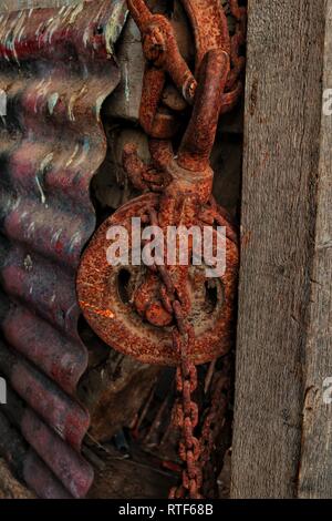 Ein rostiger Riemenscheibe und Kette langsam verfallenden in der Ecke eines Bauern Scheune. Stockfoto