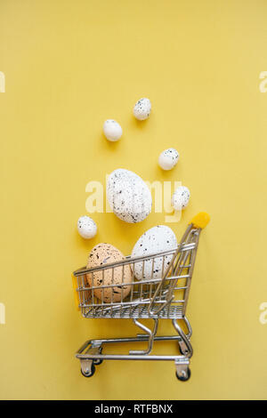 Warenkorb mit Eiern auf einem gelben Hintergrund. Das Konzept der Eine festliche Ostern Verkauf in einem minimalistischen Stil. Stockfoto