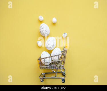 Warenkorb mit Eiern auf einem gelben Hintergrund. Das Konzept der Eine festliche Ostern Verkauf in einem minimalistischen Stil. Stockfoto