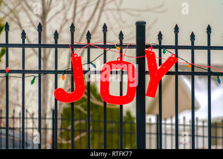 Rote Freude und Weihnachtsbeleuchtung Dekoration auf Zaun. Nahaufnahme einer lebendigen Rot Freude Dekoration hängen an einem schwarzen Zaun. Bunte Weihnachtslichter ar Stockfoto