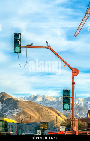 Ampel und Tower crane gegen bewölkten Himmel. Ein Verkehr Lampe mit dem grünen Licht auf gegen die schneebedeckten Berge und bewölkter Himmel. Die von einem constru Stockfoto