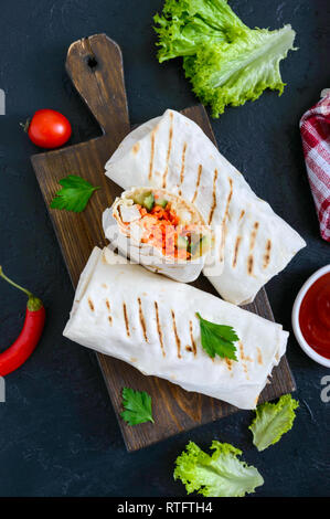 Köstliche shawarma Sandwich auf schwarzem Hintergrund. Burritos Wraps mit gegrilltem Huhn und Gemüse, Grüns. Fajitas, Fladenbrot. Traditionelle Mitte Stockfoto