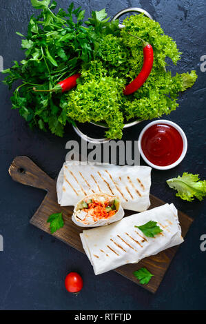 Köstliche shawarma Sandwich auf schwarzem Hintergrund. Burritos Wraps mit gegrilltem Huhn und Gemüse, Grüns. Fajitas, Fladenbrot. Traditionelle Mitte Stockfoto