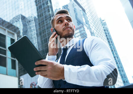Geschäftsmann mit Tablet-PC spricht über das Telefon in der großen Stadt Stockfoto