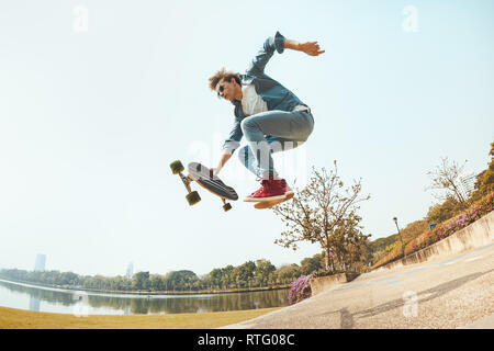 Mann hipster springt mit Skateboard in Park Stockfoto