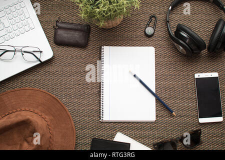 Flach. Blick von oben auf die Arbeitsfläche. Reisen oder Reiseplanung mit Notebook in der Mitte. Laptop, Handy, Portemonnaie, Kopfhörer, Notebook, Bleistift Stockfoto